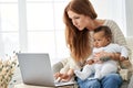 Busy mother using laptop working from home with little african baby daughter.