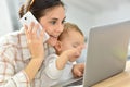 Busy young woman on laptop holding her baby