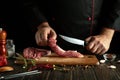 A butcher cuts veal with a knife to prepare a roast. Low key concept of cooking meat dish in saloon kitchen Royalty Free Stock Photo