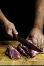 Butcher hands close up: cutting meet on wooden board on black