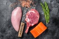 Butcher raw steaks - salmon, beef and turkey breast fillet on a meat cleaver. Black background. Top view