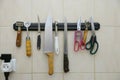 butcher's knives scisors and other kitchen utensils hanging on a rack on wall, restaurant kitchen