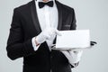 Butler in tuxedo and gloves holding blank card on tray