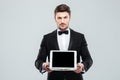 Butler in tuxedo holding blank screen tablet on tray