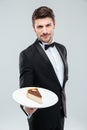 Butler in tuxedo holding piece of cake on plate