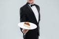 Butler in tuxedo holding plate with piece of cake Royalty Free Stock Photo