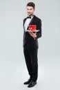 Butler in tuxedo standing and holding tray with gift box