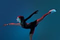 Dynamic portrait of young girl, female figure skater in black stage dress skating isolated on blue background in neon