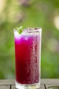 Butterfly pea juice with ice in glass, isolate on wooden table. Green leaves background. Shallow dept of field. Close. Bright