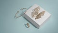 Butterfly shape golden earrings and bracelet on white box with chain shape ring on blue background
