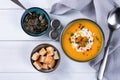 Butternut squash soup with cream, croutons, pumpkin seeds and gray napkin on one white wooden table. Copy space. Top view