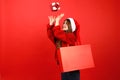Buy gifts for Christmas, sale of New Year's goods. Cheerful young woman in santa hat throws up a box on a red background