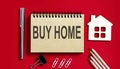 BUY HOME text written on a notebook with pencils and office tools and model wooden house Royalty Free Stock Photo