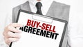 BUY-SELL AGREEMENT inscription on a notebook in the hands of a businessman on a gray background, a man points with a finger to the