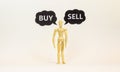 Buy or sell symbol. Wooden model of businessman human. Black paper with words `buy sell`. Beautiful white background, copy space