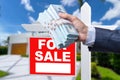 Buyer Handing Over Cash for House with Home and For Sale Real Estate Sign Behind. Royalty Free Stock Photo