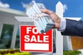 Buyer Handing Over Cash for House with Home and For Sale Real Estate Sign Behind. Royalty Free Stock Photo