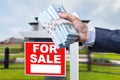 Buyer Handing Over Cash for House with Home and For Sale Real Estate Sign Behind. Royalty Free Stock Photo