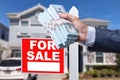 Buyer Handing Over Cash for House with Home and For Sale Real Estate Sign Behind. Royalty Free Stock Photo