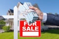 Buyer Handing Over Cash for House with Home and For Sale Real Estate Sign Behind. Royalty Free Stock Photo