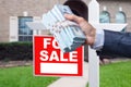 Buyer Handing Over Cash for House with Home and For Sale Real Estate Sign Behind. Royalty Free Stock Photo