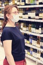 A buyer in a medical mask chooses wine in a supermarket. Sale of alcohol and drink in a store. Flu virus quarantine in public