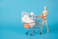 Buying hygienic products concept. Photo of wooden male figure carrying toy miniature shopping cart full of soap mask and Royalty Free Stock Photo