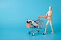 Buying new car concept. Photo of wooden male figure carrying shopping cart with mini white car inside isolated blue backdrop with Royalty Free Stock Photo