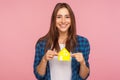 Buying property. Cheerful smiling girl in checkered shirt pleased with house bought, holding paper home