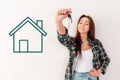 Buying and renting real estate. A woman in a plaid shirt smiles and holds a bunch of keys, a green house is painted on the wall.