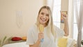 Buzzing indoor morning as beautiful blonde young woman enjoys singing fun song with brush as microphone in pajama-adorned bedroom Royalty Free Stock Photo