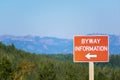 Byway information brown sign with directional arrow. Blurred landscape background with forest and mountains