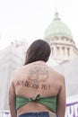 Back of a woman: a green handkerchief and a text on her skin: Here I decide