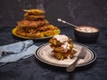 Cabbage oladi are lying on a plate, watered with sour cream, denim napkin, cutlery. In the background is a large plate with