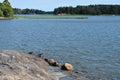 Cabin and forests across a rocky lake`s shore.