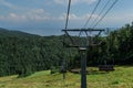 Cable car construction with empty seats among green trees, grass field in forest on hill, sunny summer blue sky with white clounds Royalty Free Stock Photo