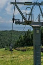 Cable car metal construction with empty seats among green trees, grass field in forest on hill, sunny summer blue sky Royalty Free Stock Photo