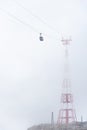 A cable car, mountain gondola suspended on a rope disappearing in the fog. The red-white pylon steel construction is barely visibl Royalty Free Stock Photo