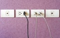 Cables plugged in a white electric outlet mounted on pink wall Royalty Free Stock Photo