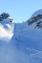 Cableway in the snowy mountains on the background of the blue sky. Slope with traces of skis and snowboarding lovers of