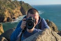 A young photographer takes a photo near a cliff against the background of the Atlantic Ocean on a Nikon D810 camera