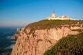 Cabo da Roca, Portugal - March, 2019: white lighthouse on cliffs with green grass at evening time.