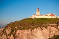 Cabo da Roca, Portugal - March, 2019: white lighthouse on cliffs with green grass at evening time.