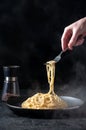 Cacio e Pepe - Hot Italian Pasta with Cheese and Pepper on Black Plate, Woman Holding Fork Spaghetti on Dark Background