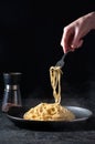 Cacio e Pepe - Hot Italian Pasta with Cheese and Pepper on Black Plate, Woman Holding Fork Spaghetti on Dark Background Royalty Free Stock Photo