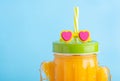 Cactus shape mason jar with orange juice. A jar with green lid and straw with sunglasses.