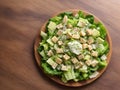 Caesar salad with grilled chicken meat, lettuce and cheese, shot from the top on the wooden table background