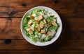 Caesar salad with grilled chicken meat, lettuce and cheese, shot from the top on the wooden table background