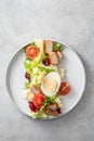 Caesar salad in modern linear feed with chicken, egg, tomatoes, lettuce and parmesan chips isolated on gray table, top