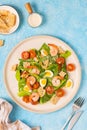 Caesar salad with romaine lettuce, cherry tomatoes, boiled quail eggs and croutons on a light ceramic plate on a blue concrete Royalty Free Stock Photo